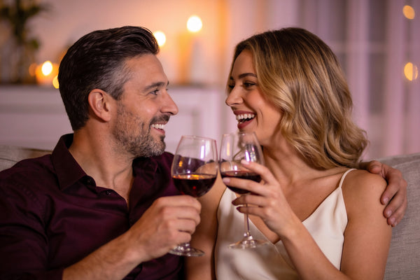 Cuplu pe canapea, cu pahare de vin, vorbind apropiat și râzând seara