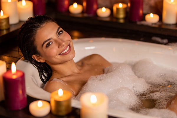 Femeie relaxată într-o cadă cu spumă, la lumina lumânărilor, zâmbind