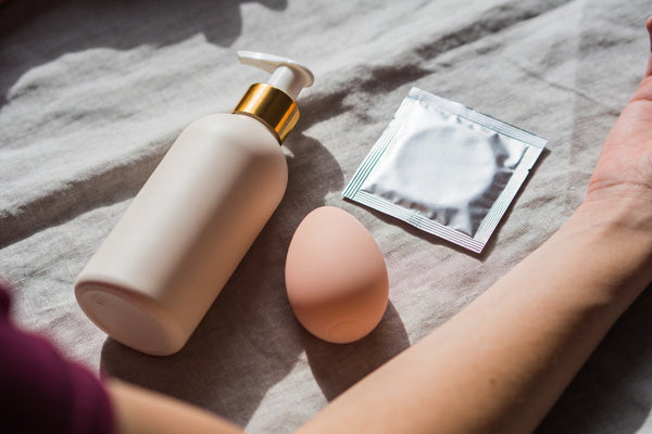 Flacon de lubrifiant, vibrator pastel din silicon și prezervativ pe lenjerie gri